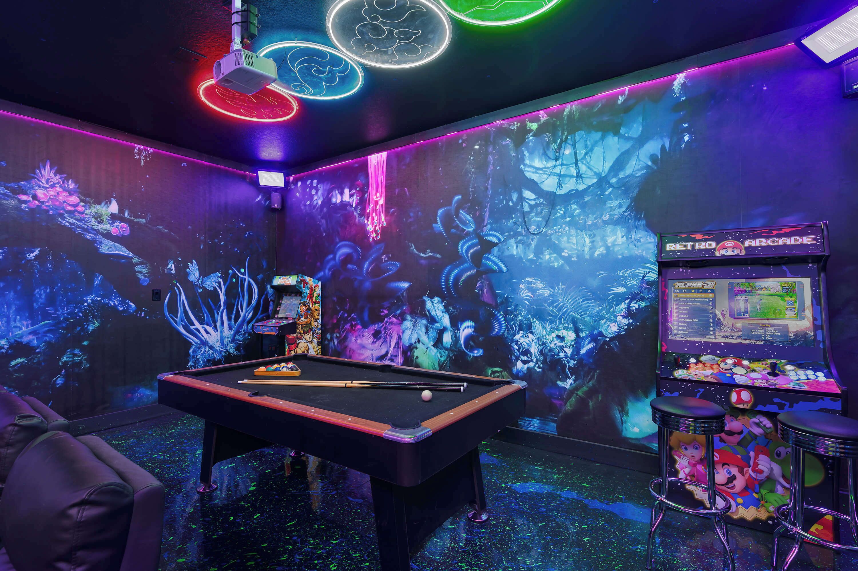 Uma mesa de bilhar com uma máquina de jogos eletrônicos iluminada por neon e uma grande projeção na parede.