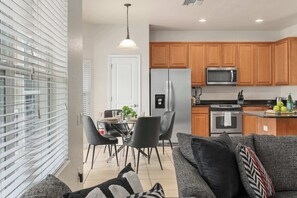 A modern kitchen with wooden cabinets, a stainless steel refrigerator, a microwave, and a dining area with a table and chairs. - Themed House with Heated Private Pool & Game Room (Kissimmee)