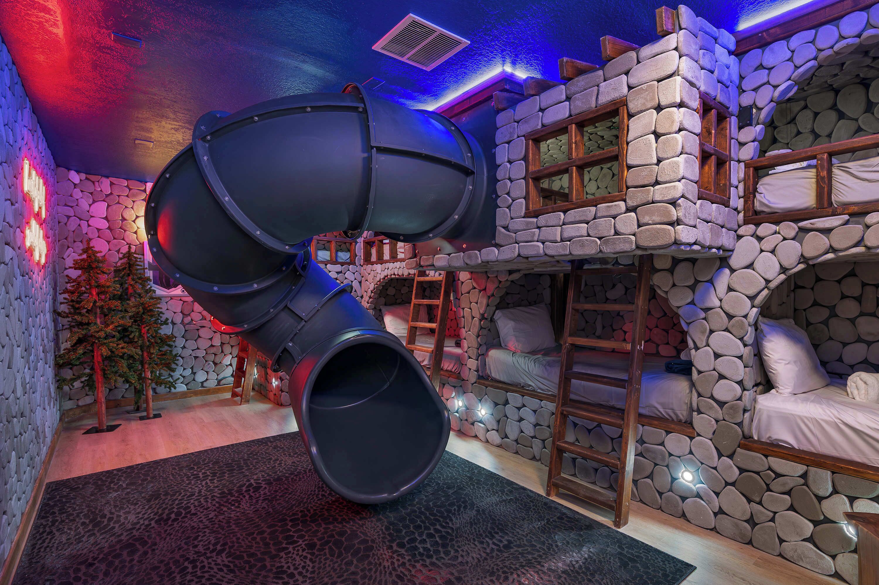 A room with a large slide, bunk beds, and a stone wall.