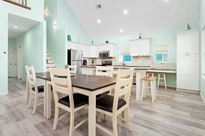 Una cocina moderna con armarios blancos, una mesa de comedor con sillas y un horno empotrado.