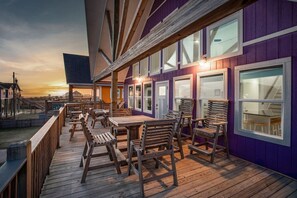 Eine Terrasse im Freien mit Holzmöbeln und einem violetten Gebäude mit großen Fenstern.