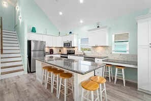 A kitchen with a central island, bar stools, white cabinets, a stainless steel refrigerator, and a microwave. - The Luxe Coast House -  Walk to the Beach (Bolivar Peninsula)