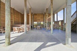 Un espacio interior diáfano con techos altos y vigas de madera, que presenta una zona de estar central y grandes ventanales.