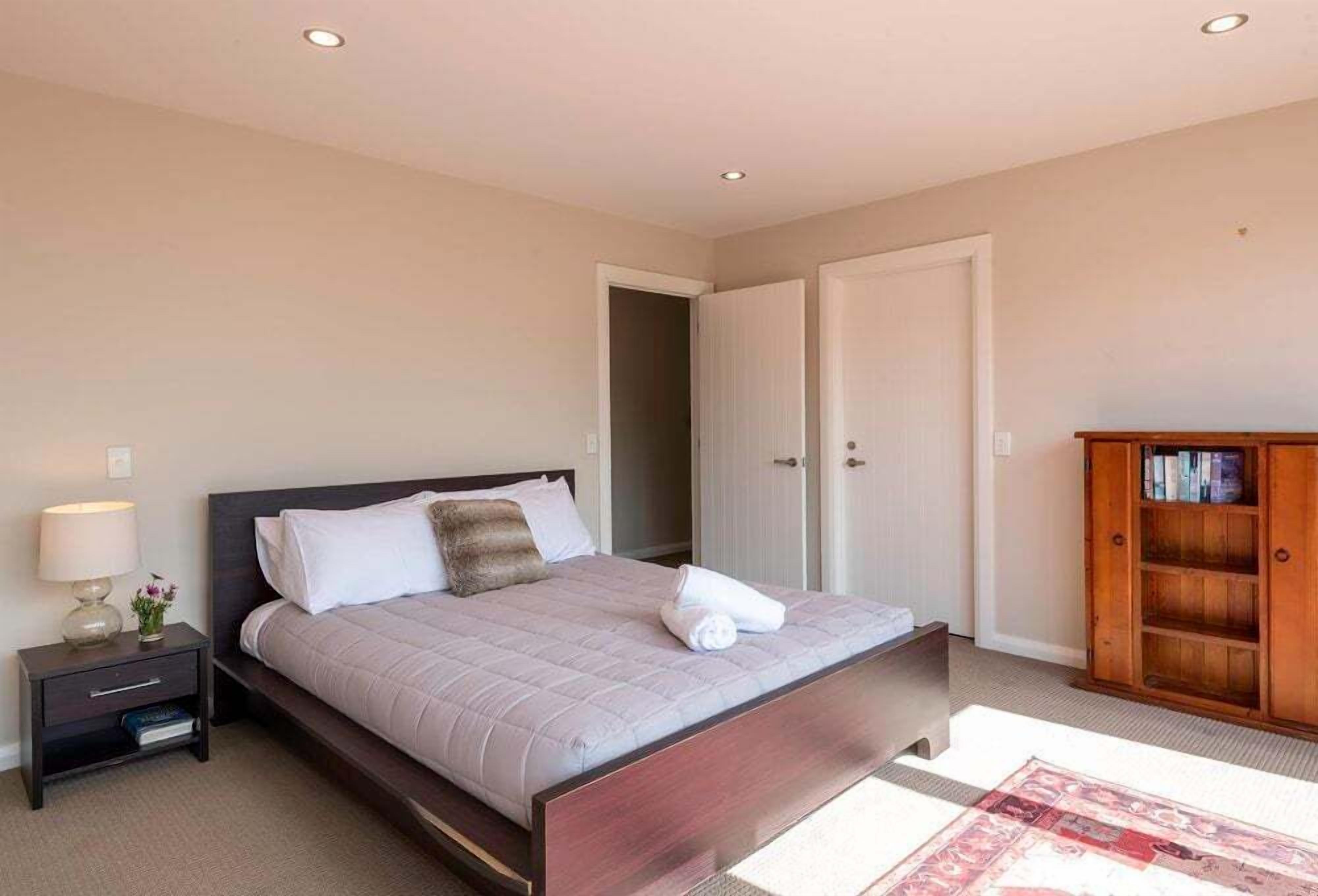 Ein Schlafzimmer mit Bett, Nachttisch, Lampe und einem Holzschrank.