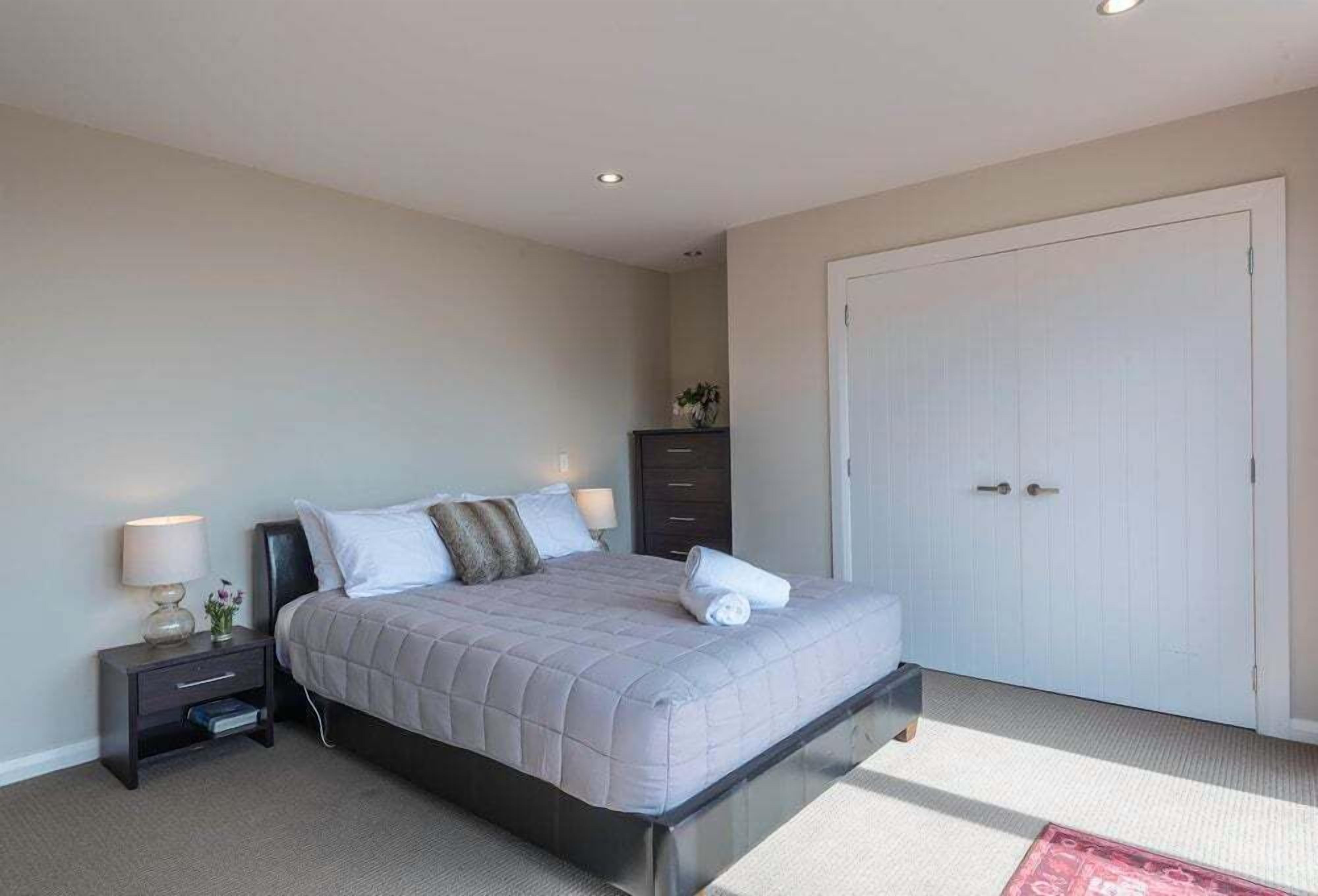 A bedroom with a bed, nightstand, dresser, and a door.