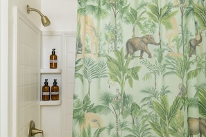 A bathroom with a shower curtain featuring a jungle print, a showerhead, and two bottles of shampoo on a shelf. - Charming Studio in perfect Marina del Rey with cool AC (Marina del Rey)