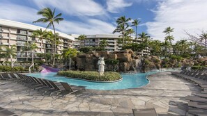 Une piscine de complexe hôtelier avec des chaises longues, des palmiers et une cascade.