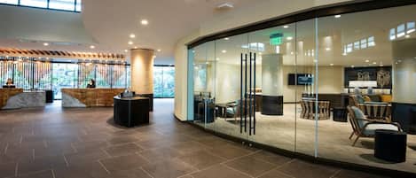 A modern lobby with a reception desk, seating area, and a glass wall offering a view of the outdoors.