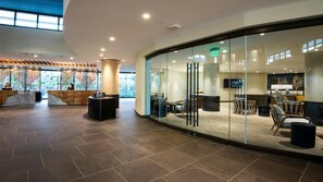Eine moderne Lobby mit Empfangsschalter, Sitzgelegenheiten und einer Glaswand mit Blick ins Freie.