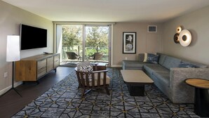 A modern living room with a flat-screen TV, a sofa, a patterned rug, and a balcony with chairs.