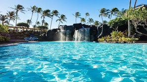 Ein Pool mit klarem, blauem Wasser, Palmen und einem Wasserfall.