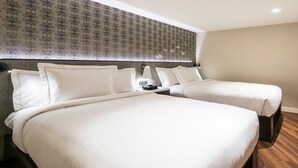 A hotel room with two beds, a patterned wallpaper, a nightstand with a lamp, and a wooden floor.
