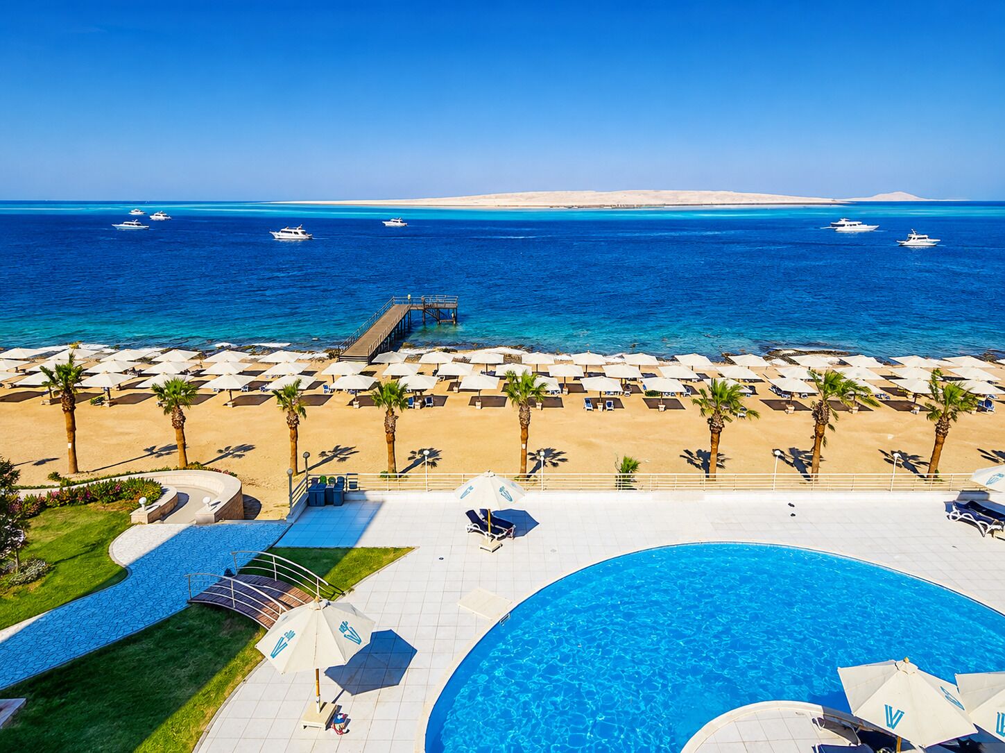 A resort with a pool, beach umbrellas, and a view of the sea.
