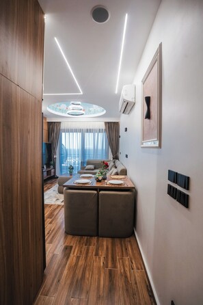 A modern interior with a wooden floor, a dining area with a table set for two, and a living area with a sofa and a TV. - Blue Haven H 101 Nubian The view Hurghada (hurghada)