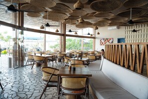 A restaurant interior with wicker furniture, large windows, and a tiled floor. - Blue Haven H 101 Nubian The view Hurghada (hurghada)