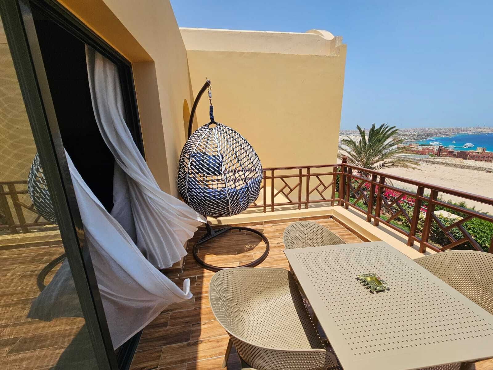 Een balkon met een tafel en stoelen, een hangstoel en uitzicht op het strand en de skyline.