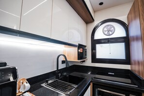 Una cocina compacta con microondas, lavamanos y una ventana con vista circular.