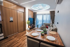 A modern living room with a wooden floor, a sofa, a dining table set for two, and a large window with curtains. - Blue Haven H 101 Nubian The view Hurghada (hurghada)