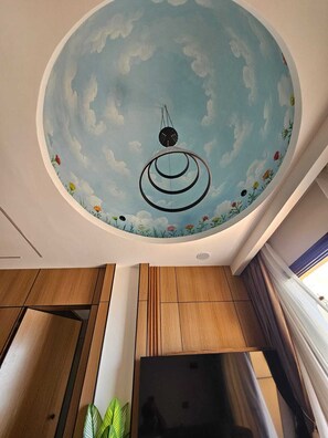 Una habitación con un mural circular en el techo que muestra un cielo con nubes y un objeto suspendido.