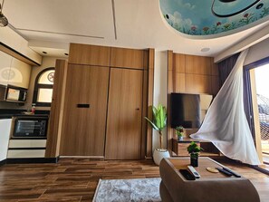 A modern living room with a sofa, a flat-screen TV, and a dining area with wooden cabinets and a microwave. - Blue Haven H 101 Nubian The view Hurghada (hurghada)