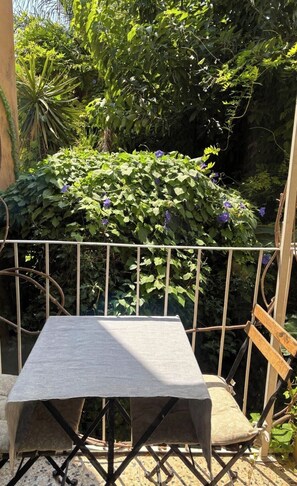 Ein Sitzbereich im Freien mit Tisch und Stühlen, umgeben von einem Metallzaun und üppiger Bepflanzung.
