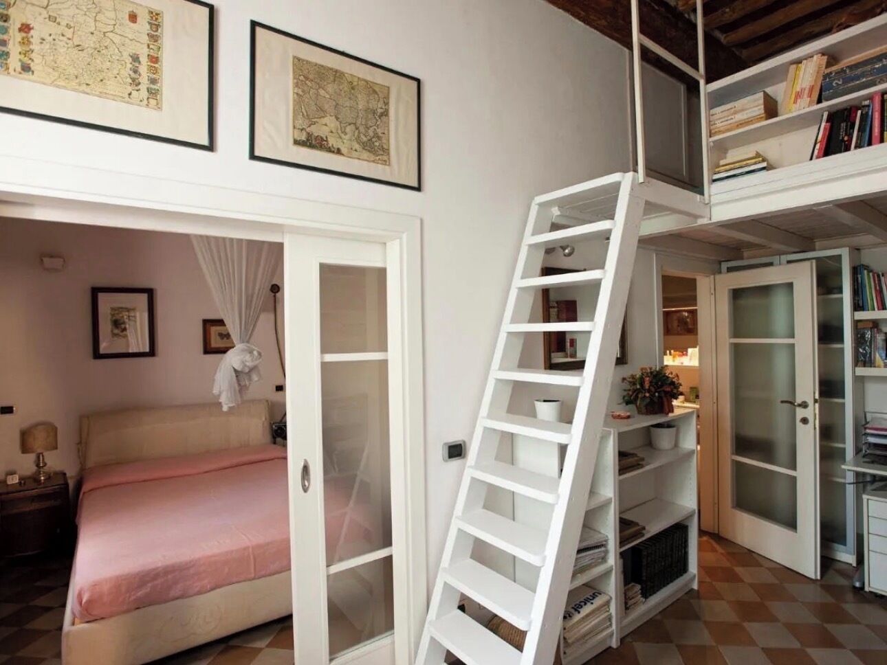 A bedroom with a bed, a ladder leading to a lofted area with bookshelves, and a map on the wall.