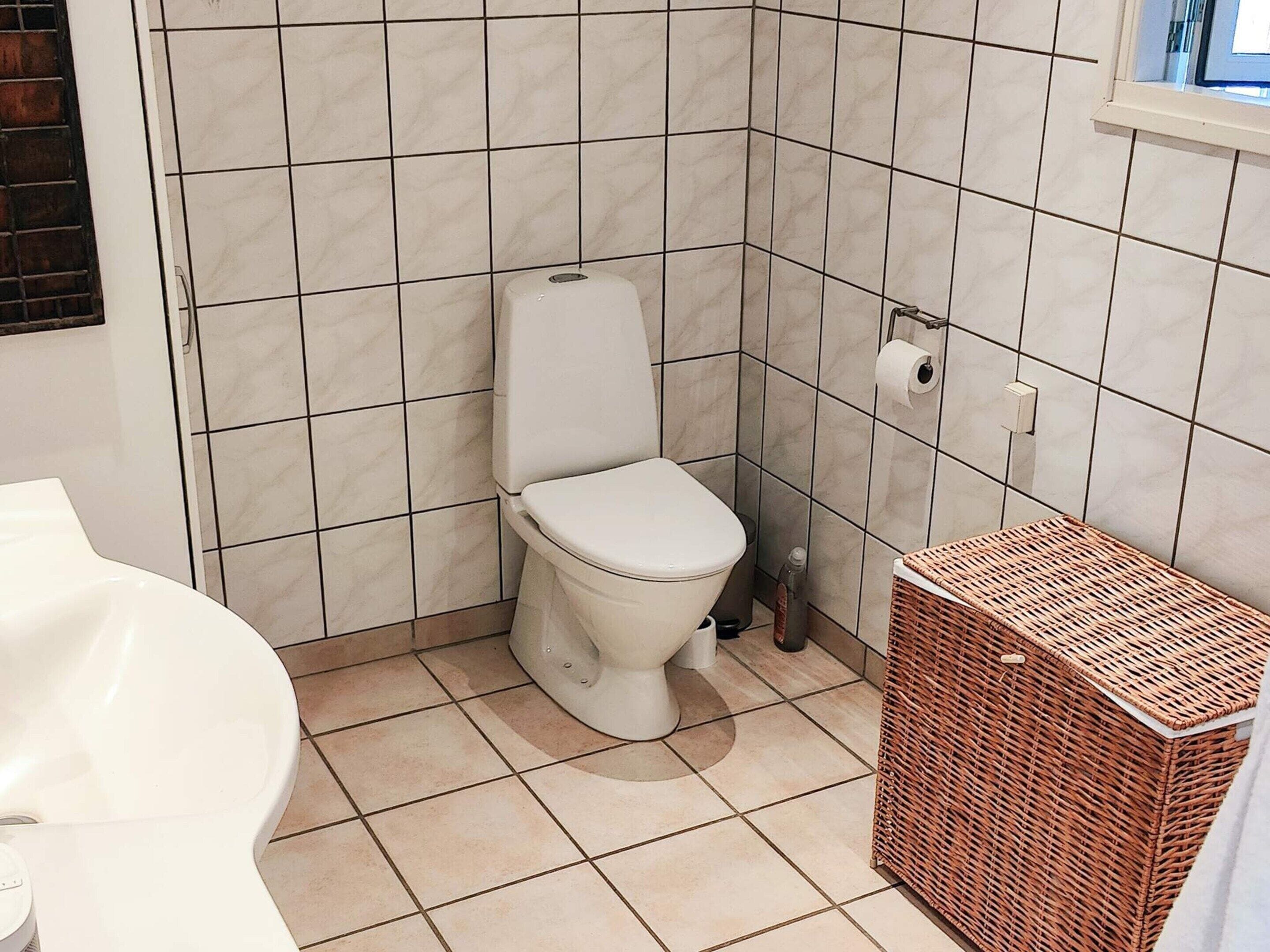Ein Badezimmer mit Toilette, Toilettenpapier, einem Korbwannenaufsatz und einer Badewanne.