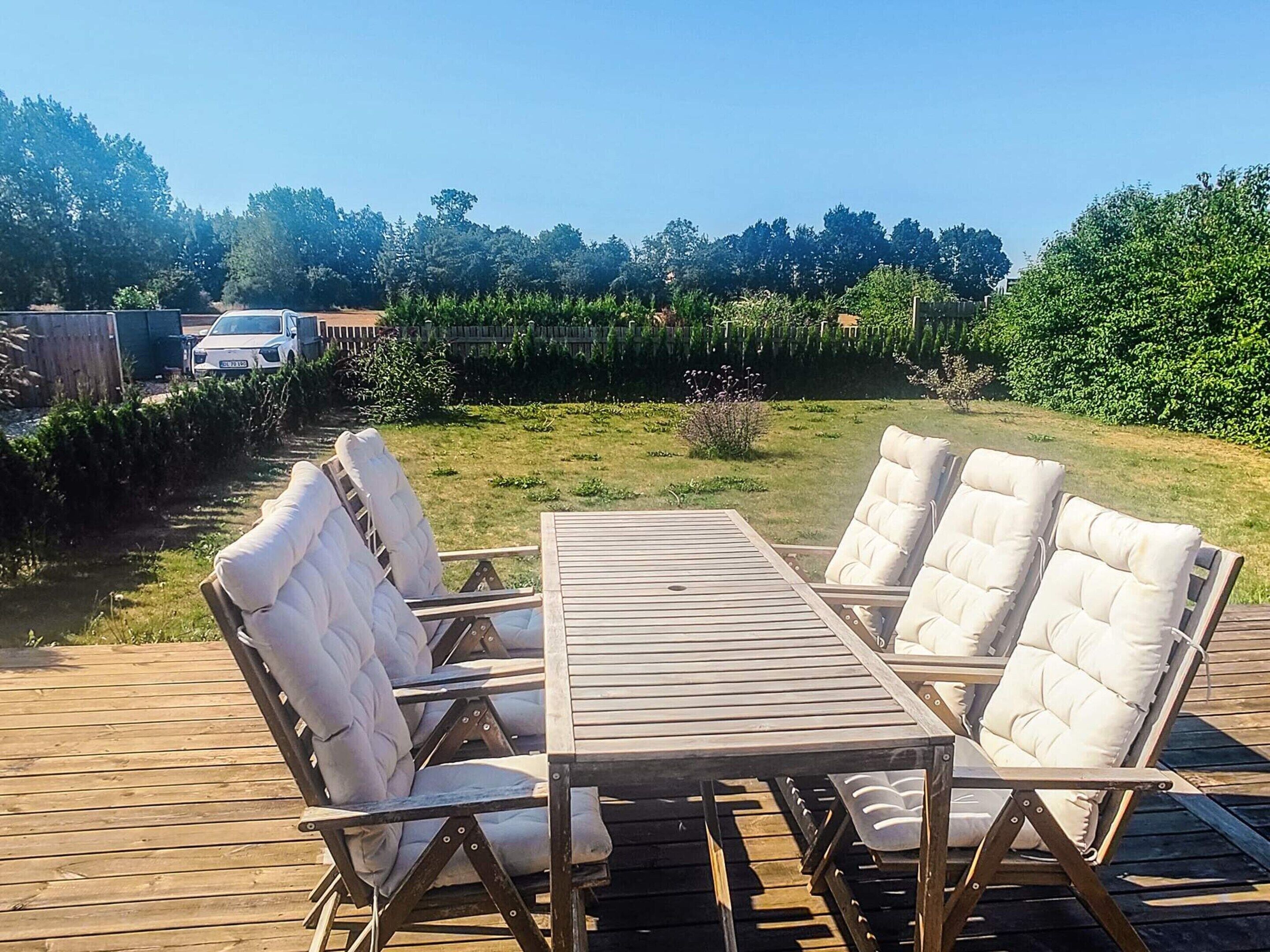 Una terraza de madera con una mesa y cuatro sillas acolchadas.