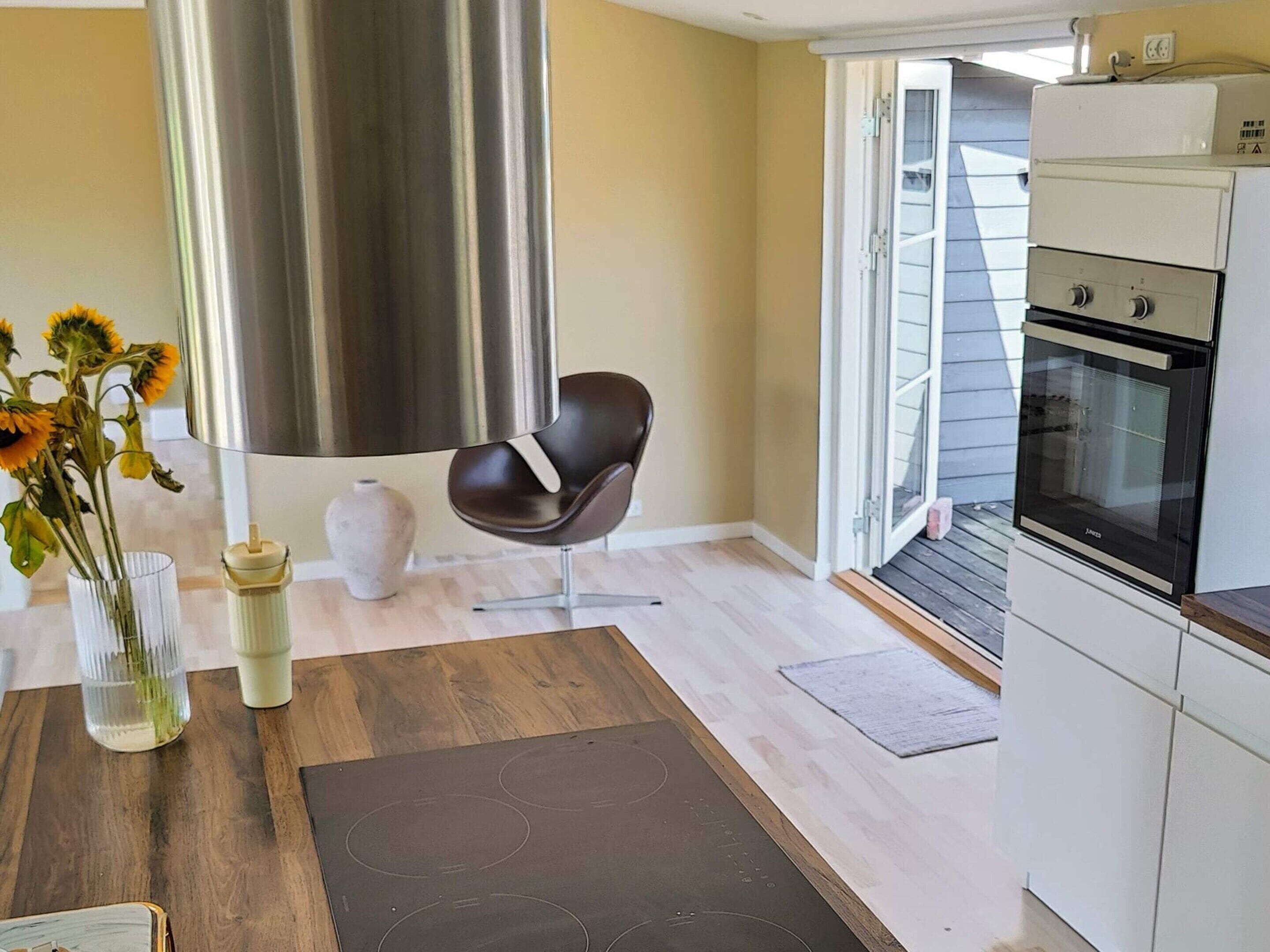 A modern kitchen with a built-in oven, a dining area with a wooden table and a vase of sunflowers, and a large window with a view of the outside.