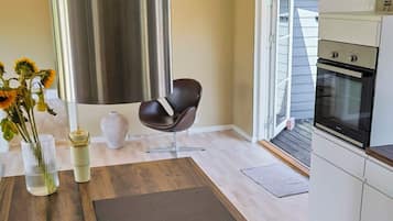 Una cocina moderna con horno integrado, un comedor con mesa de madera y un jarrón de girasoles, y un ventanal con vistas al exterior.