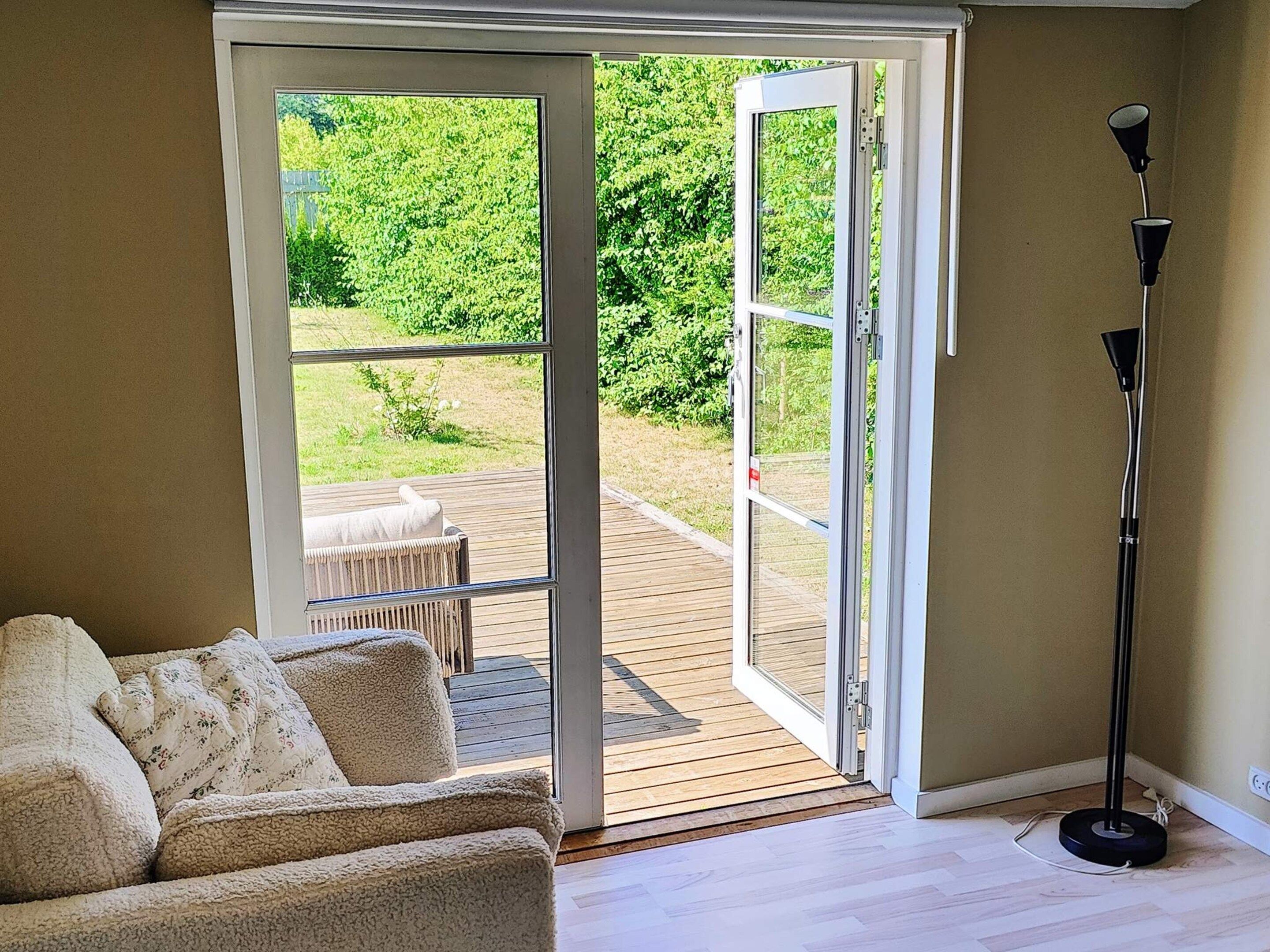 A room with a sliding glass door leading to an outdoor deck, a sofa, and a floor lamp.