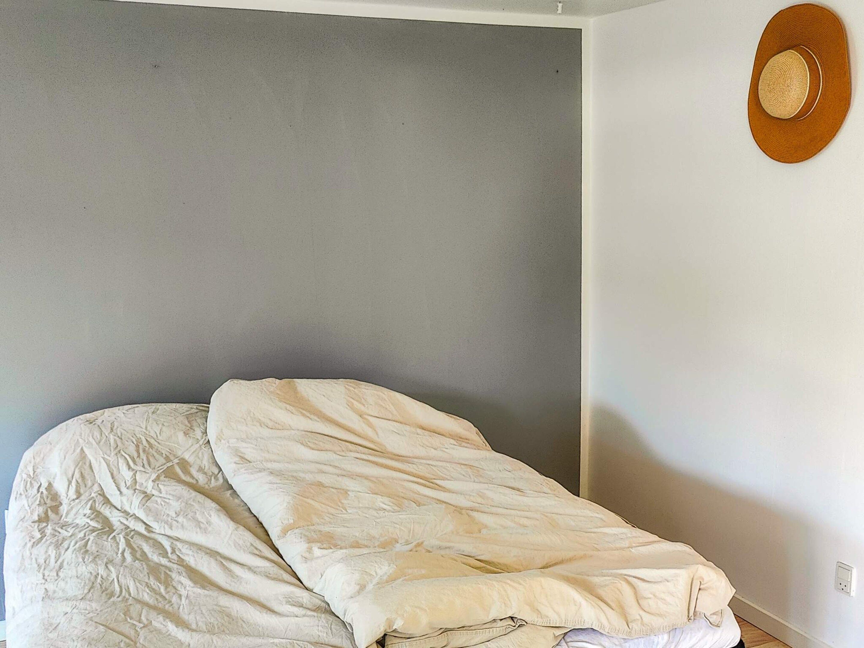 A single bed in a room with a plain wall and a hat hanging on the wall.