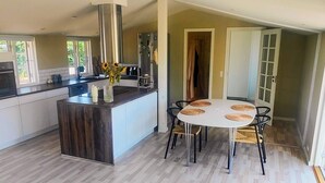 Una cocina moderna con una isla central, una zona de comedor con mesas redondas y vistas al exterior.