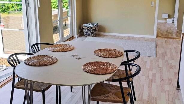 Un comedor con una mesa redonda, cuatro sillas, individuales tejidos y vistas a un patio exterior a través de un ventanal.