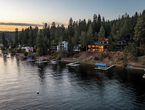 A waterfront property with docked boats, a house with a blue roof, and a forested hillside.