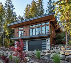 A modern two-story house with a garage, surrounded by a natural landscape with trees and rocks.