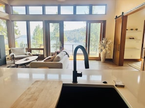 A modern kitchen with a large island, a dining area with a sofa and chairs, and a view of a lake through large windows.