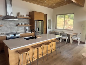 A modern kitchen with a central island, bar stools, and a dining area with chairs.