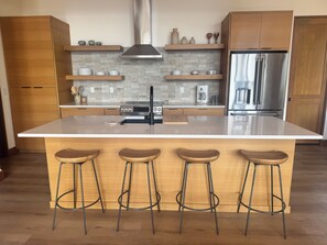 A modern kitchen with a central island, bar stools, wooden cabinets, and stainless steel appliances.
