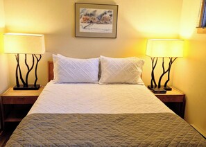 Ein Hotelzimmer mit einem Bett, zwei Nachttischen, zwei Lampen und einem gerahmten Bild an der Wand.