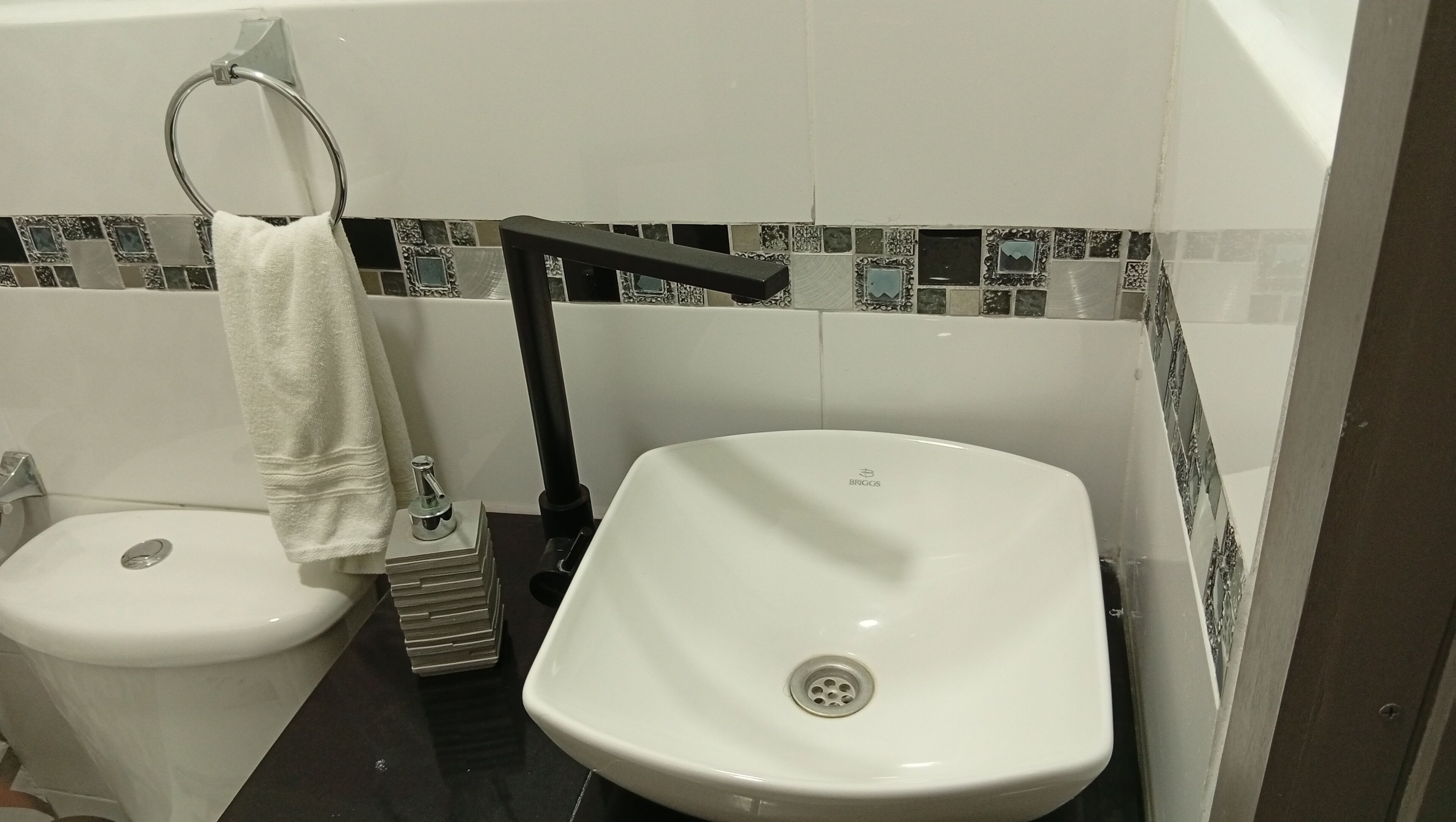 Un baño con inodoro y lavamanos blancos, y un perchero para toallas.