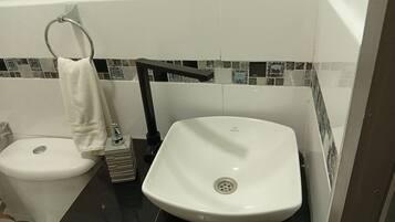 Un baño con inodoro y lavamanos blancos, y un perchero para toallas.