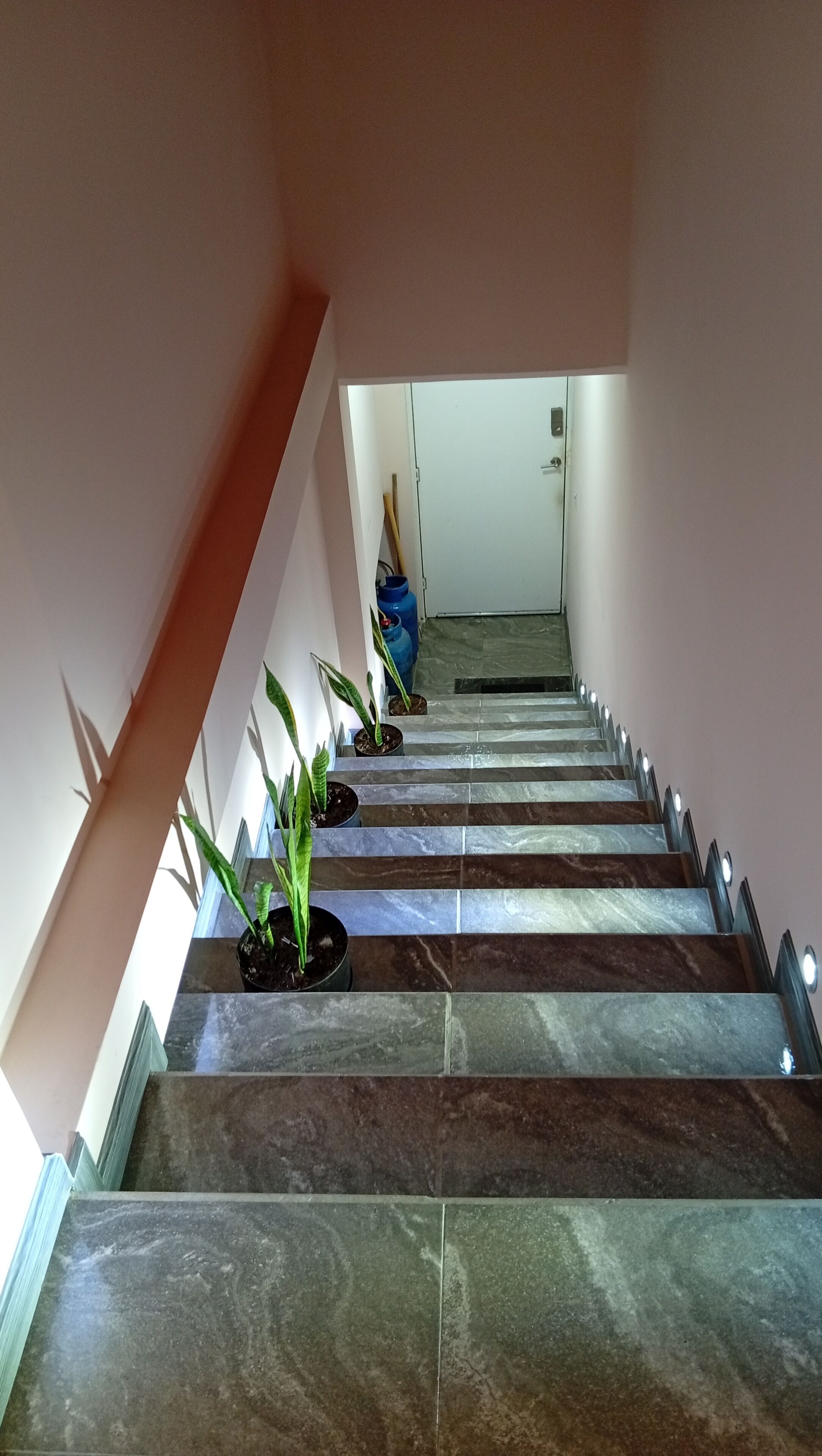 Una escalera con baldosas alternadas en tonos oscuros y claros, que lleva a una puerta en la parte superior.