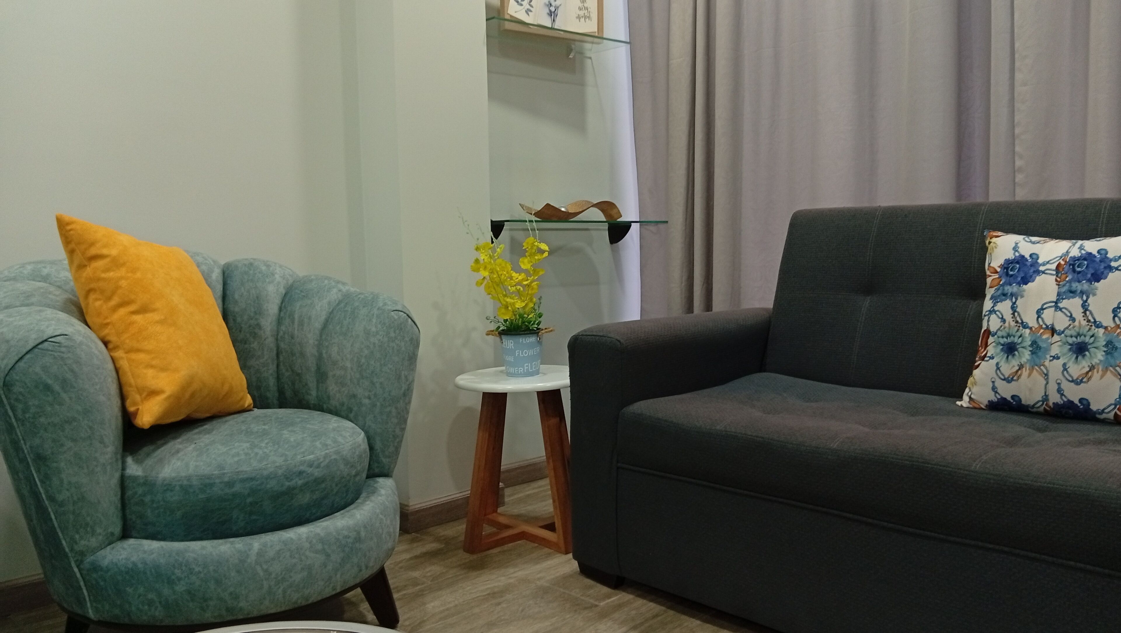 Una sala de estar con un sillón verde azulado, un sofá oscuro y una mesita auxiliar con una planta en maceta.
