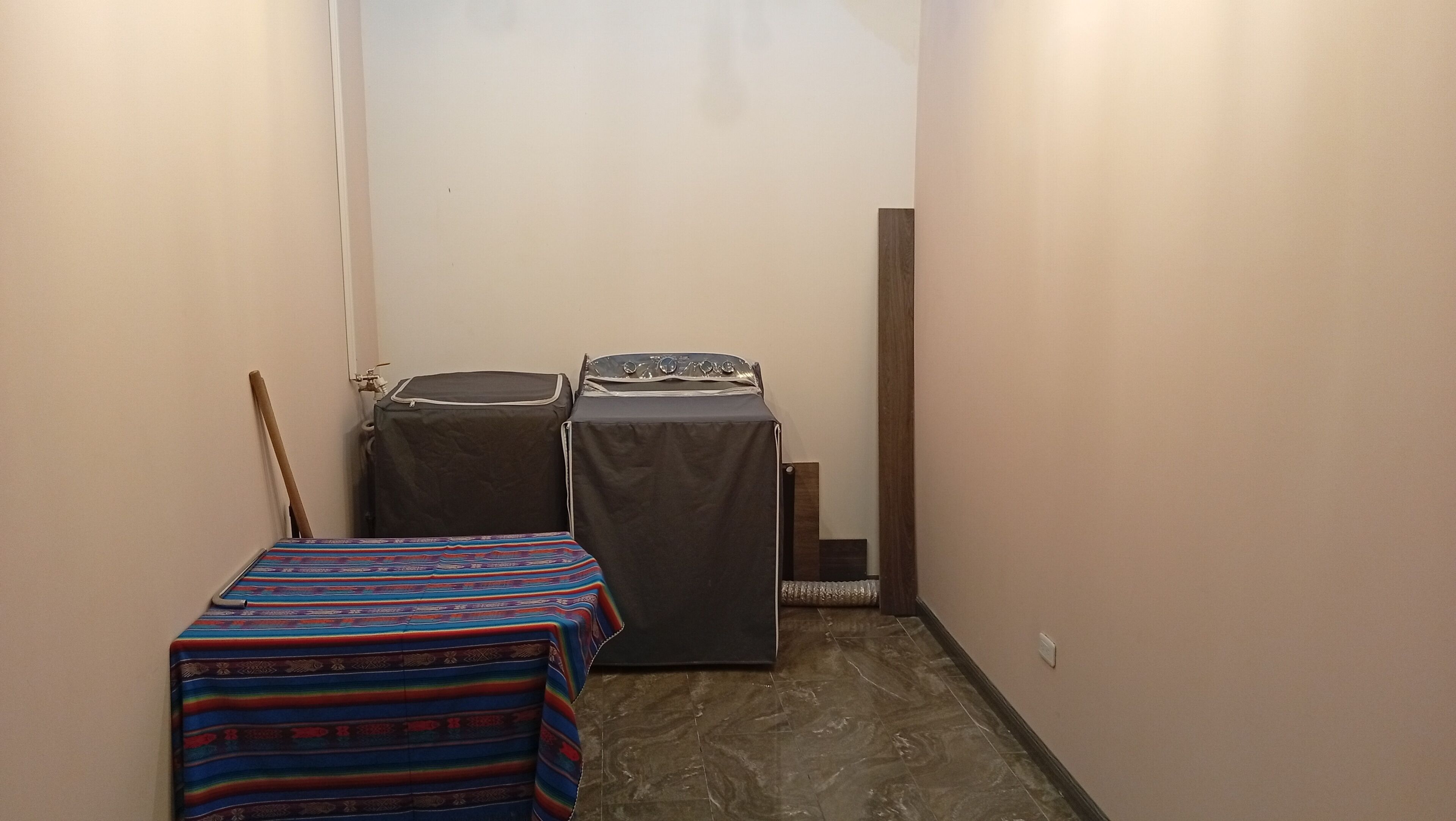 A narrow hallway with a bed, a washing machine, and a dryer against the wall.