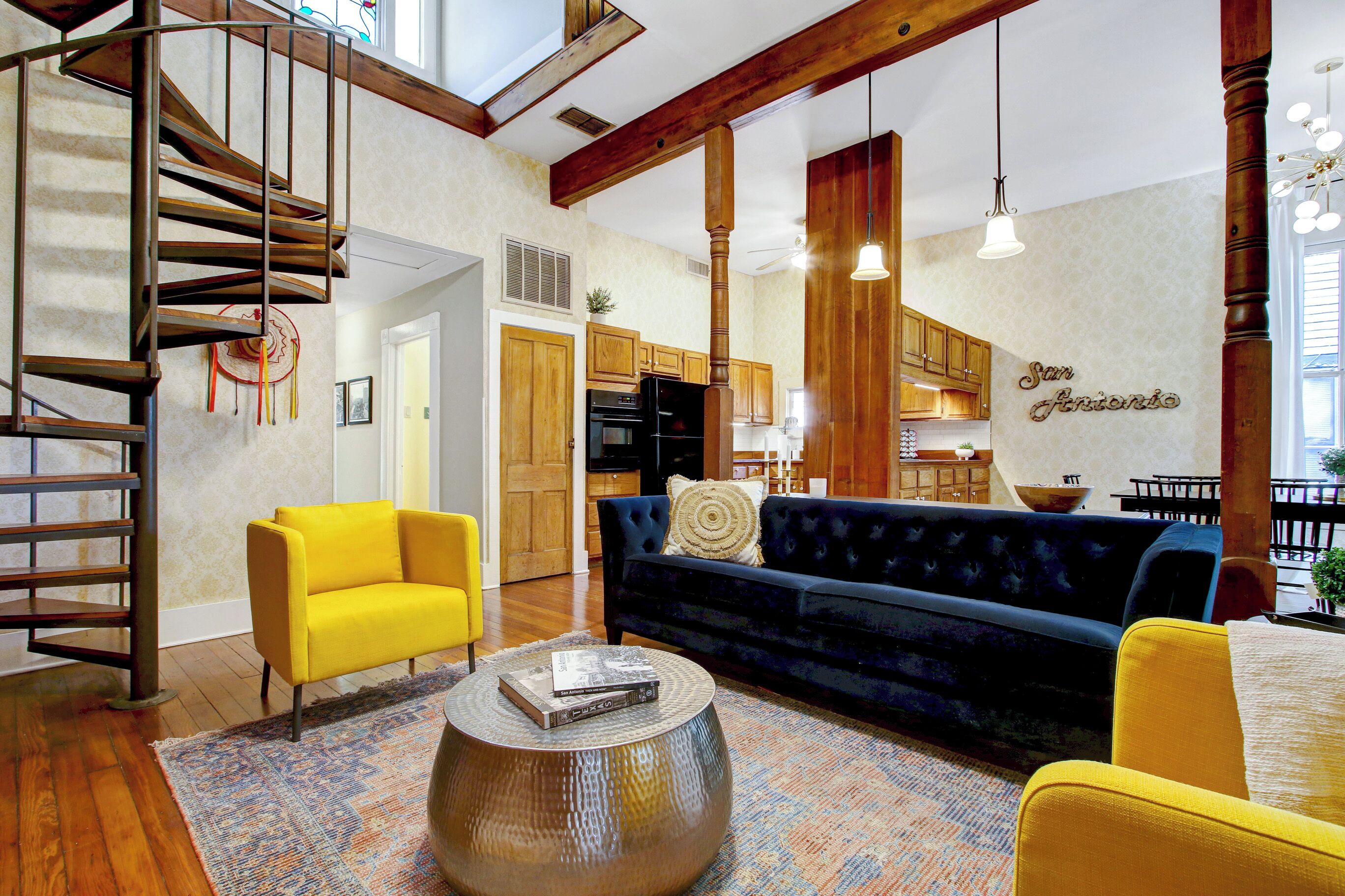 Un salon spacieux avec un escalier en colimaçon, un canapé bleu, un fauteuil jaune et une table basse ronde.