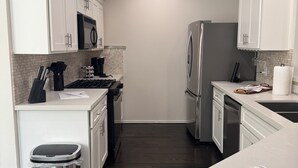Uma cozinha moderna com armários brancos, eletrodomésticos de aço inoxidável e piso de madeira escura.