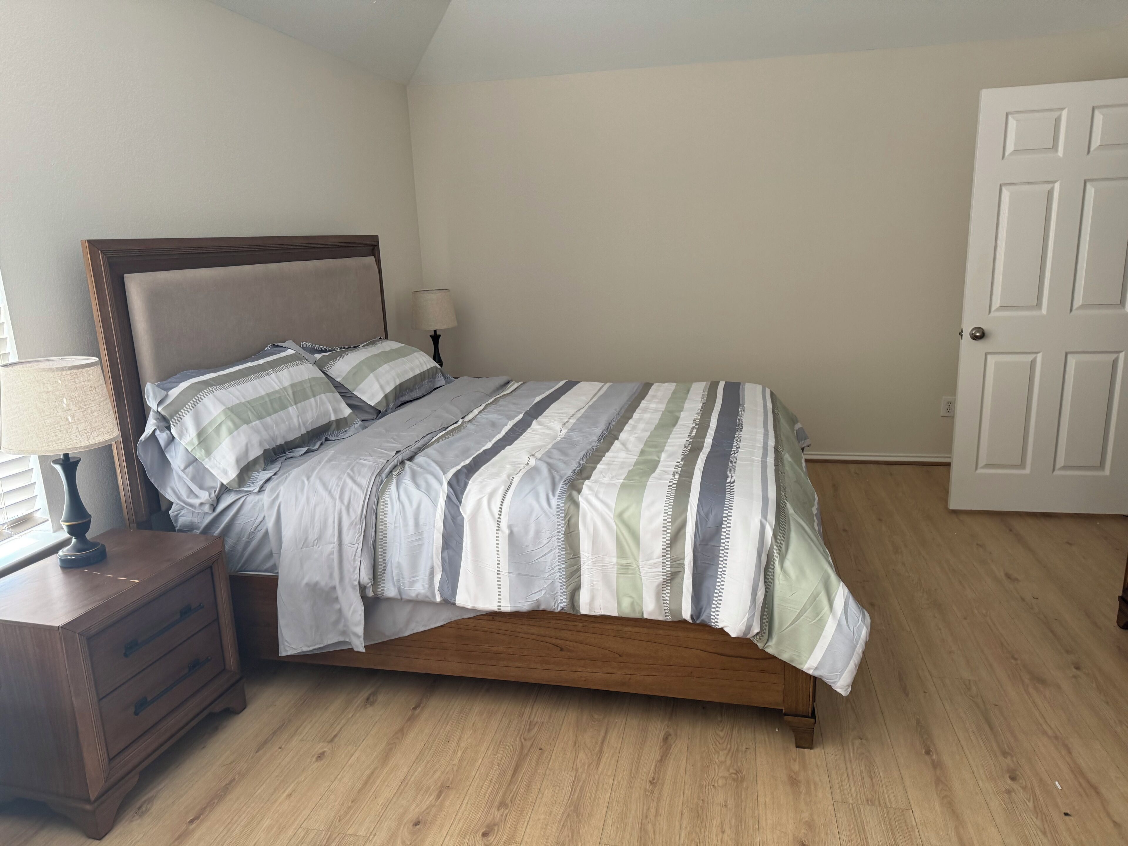 Un dormitorio con una cama de madera, una mesita de noche con lámpara y una puerta.