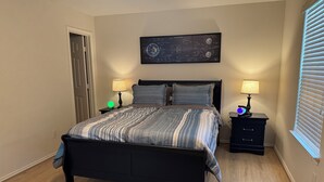 Um quarto com uma cama, duas mesas de cabeceira, um relógio na parede e uma janela com persianas.