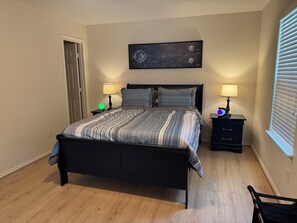 Ein Schlafzimmer mit einem Bett, zwei Nachttischen, einer Wanduhr und einem Fenster mit Jalousien.